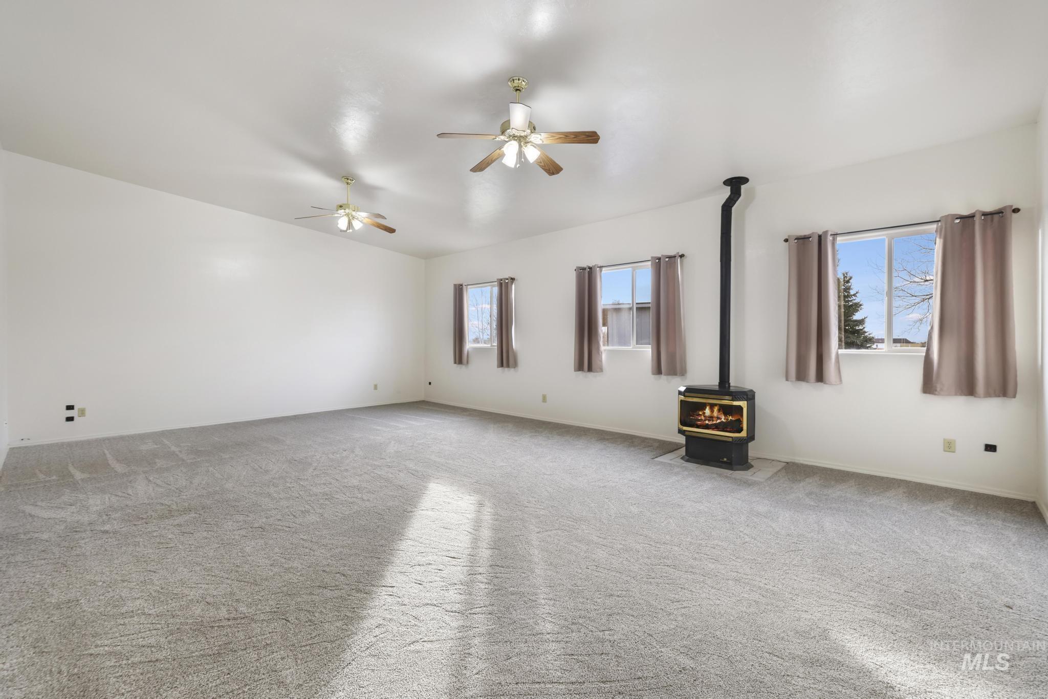 Empty room with a wood stove, carpet, and a ceiling fan