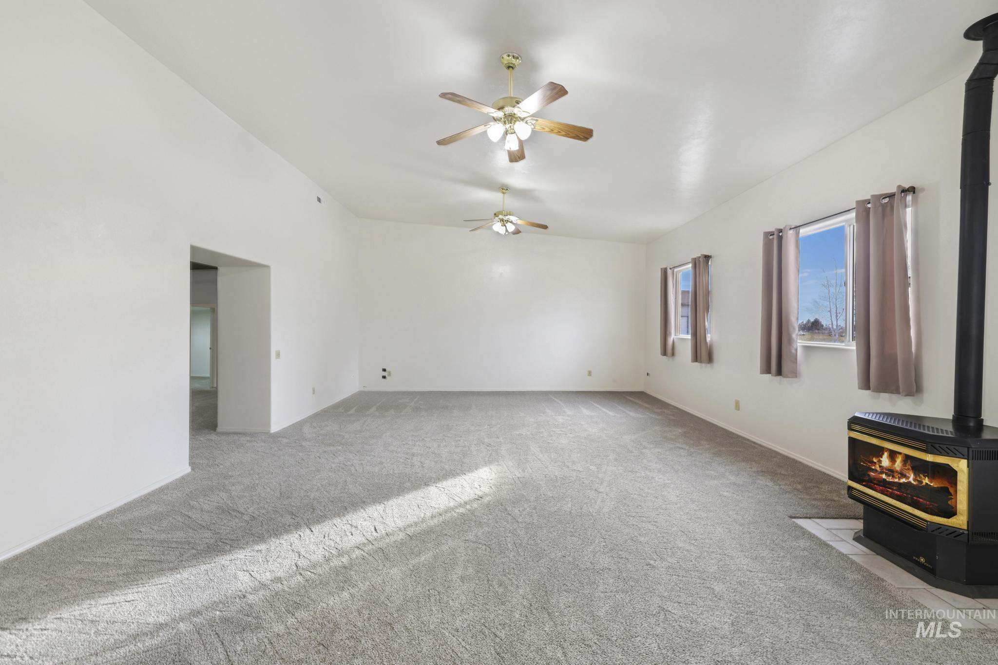 Unfurnished living room featuring a wood stove, light colored carpet, and ceiling fan