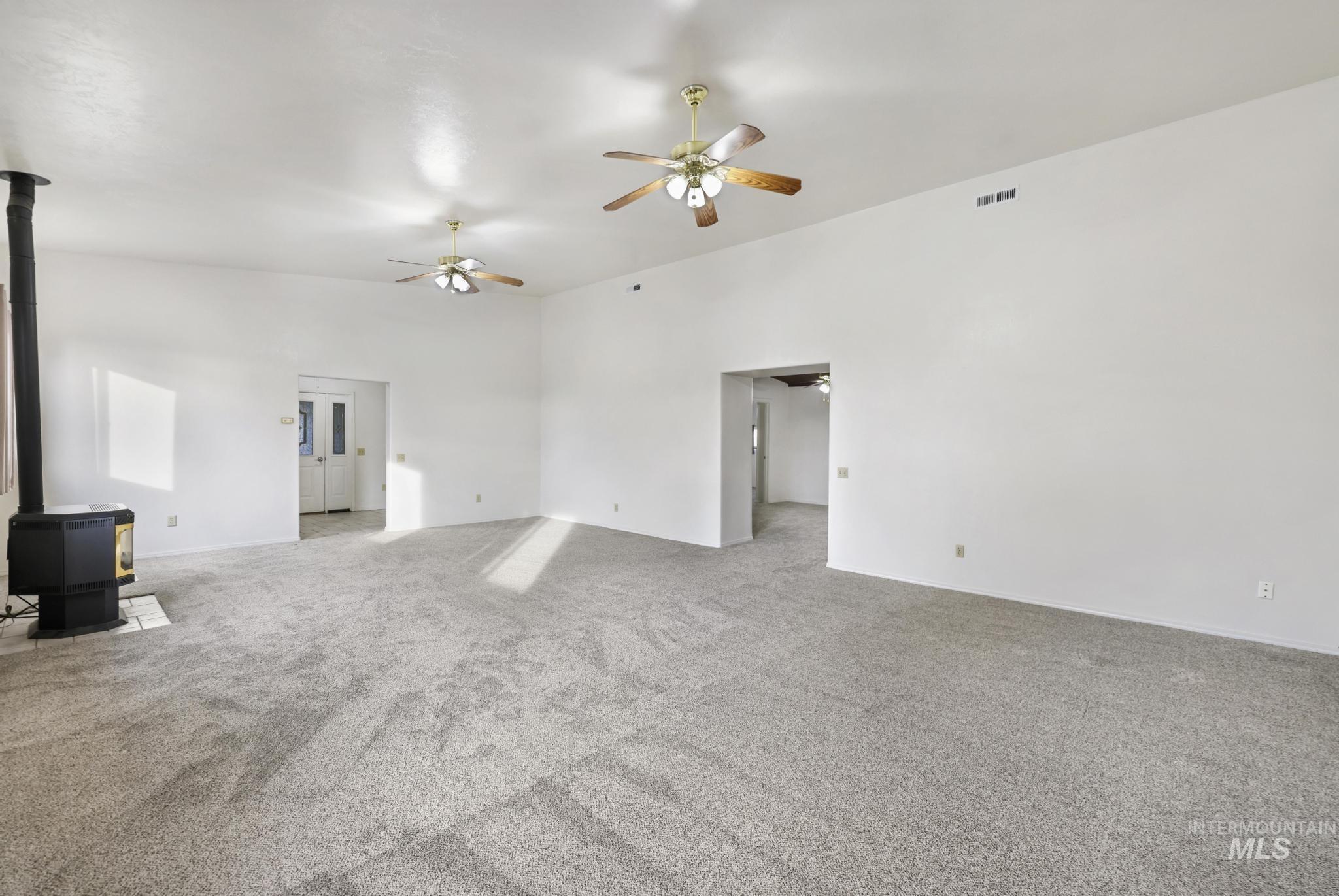 Unfurnished living room with a wood stove, light carpet, and a ceiling fan