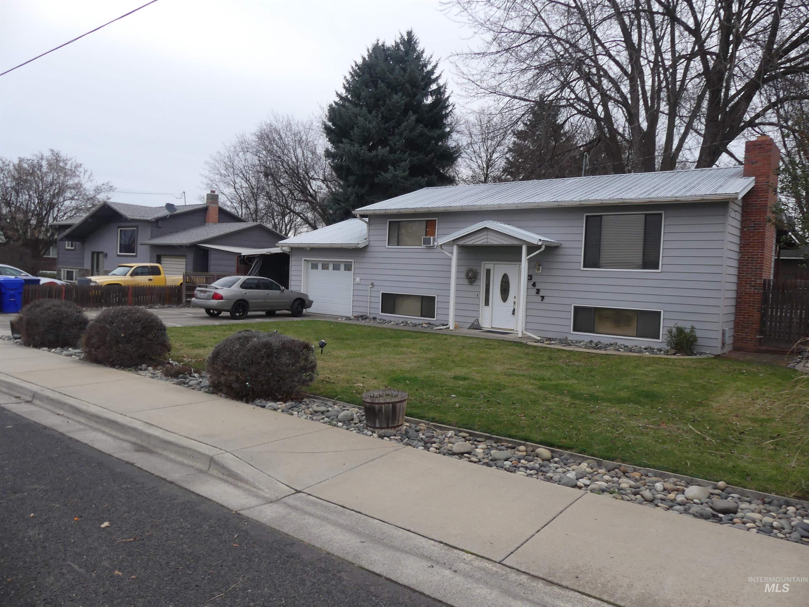 Raised ranch featuring a front yard, a chimney, an attached garage, and driveway