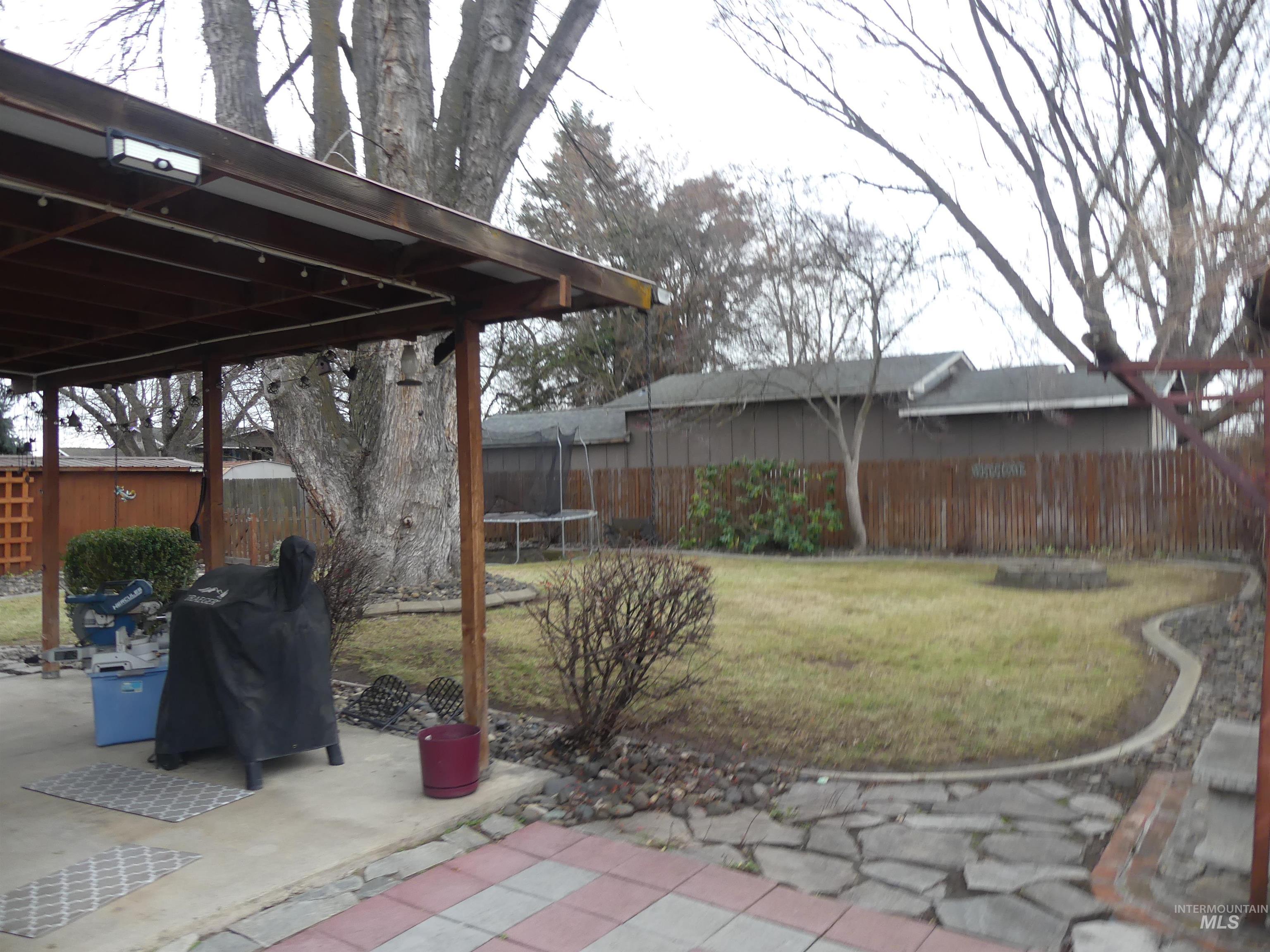 Fenced backyard with a trampoline, a grill, and a patio area