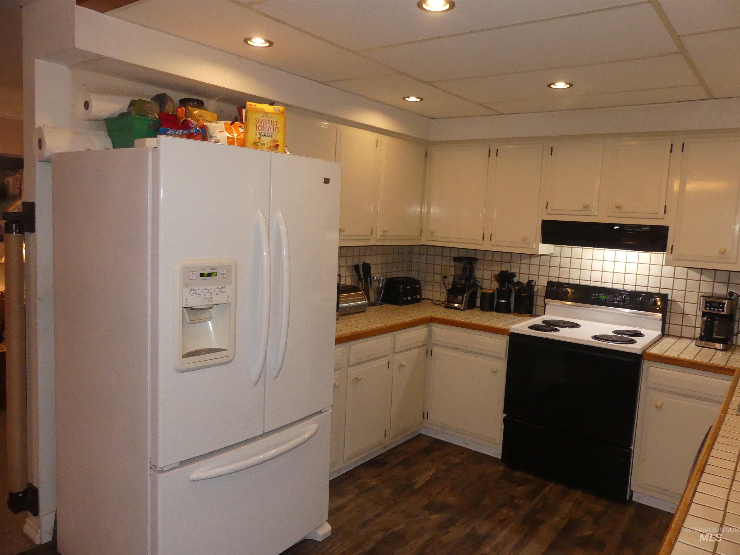 Kitchen featuring white refrigerator with ice dispenser, range with electric cooktop, white cabinets, tile countertops, and dark wood-style floors