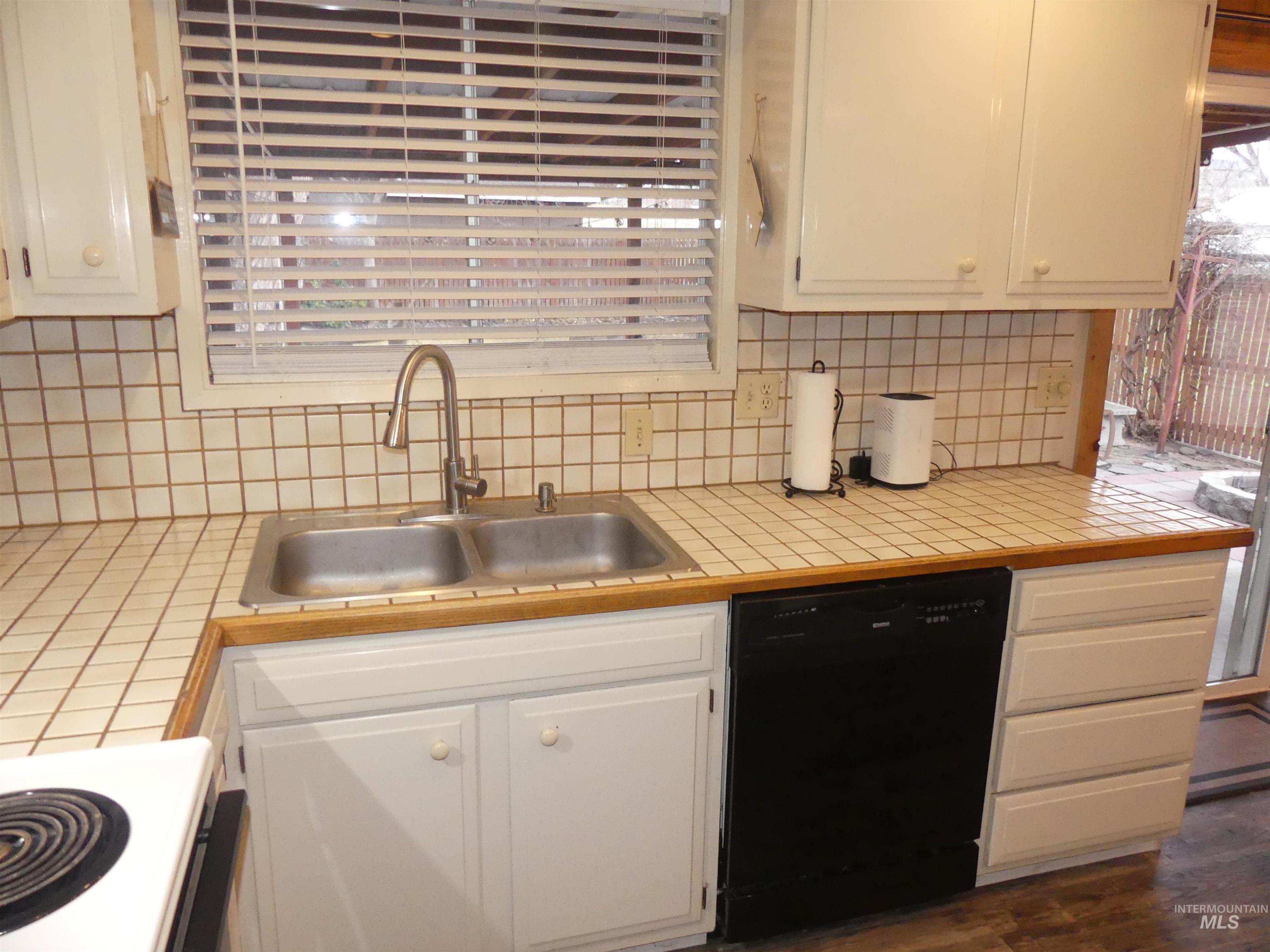 Kitchen with tile counters, black dishwasher, white electric range, tasteful backsplash, and white cabinets