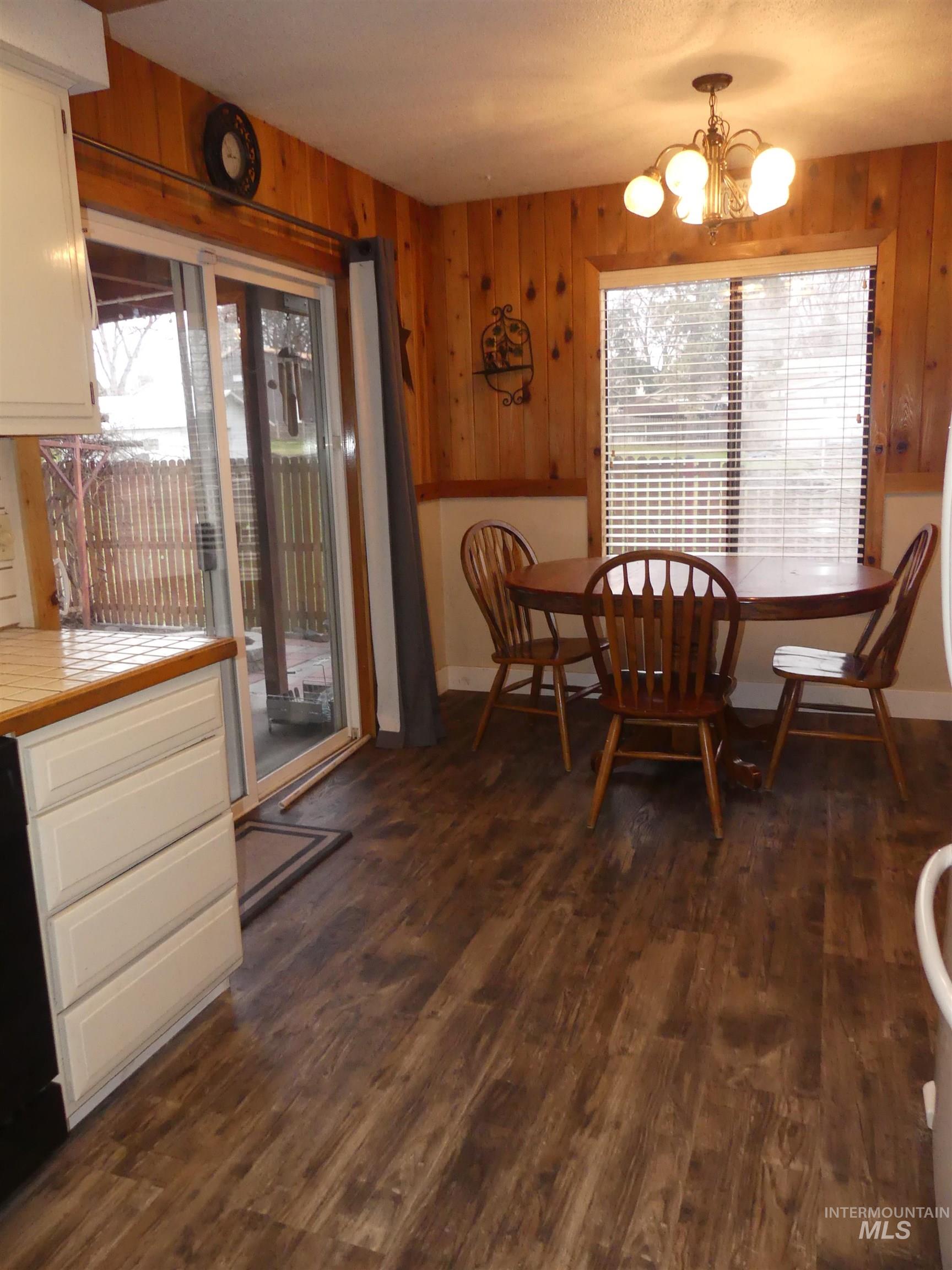 Dining room featuring healthy amount of natural light, dark wood-type flooring, wooden walls, and a chandelier