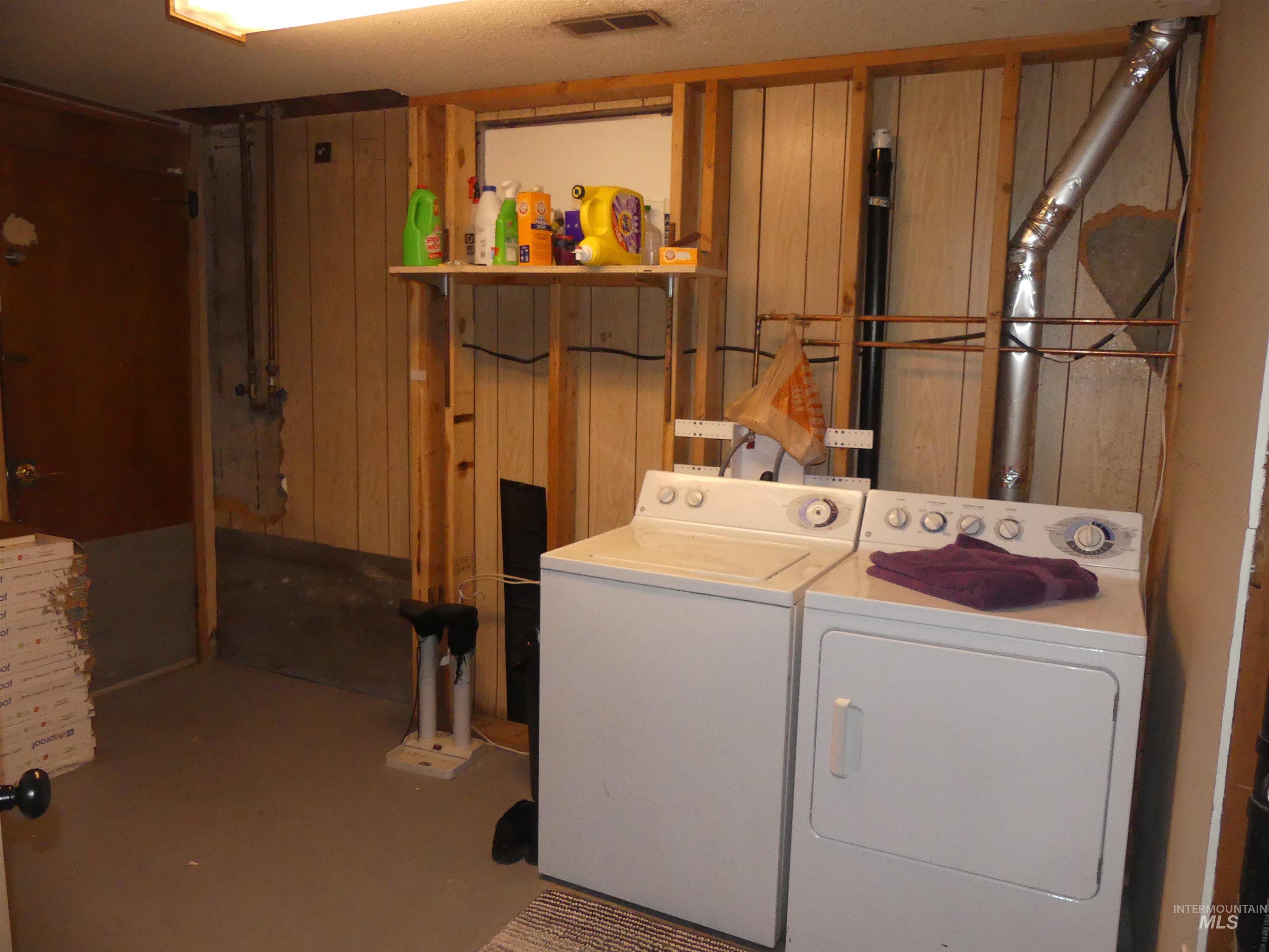 Washroom with concrete flooring, washer and dryer, wooden walls, and a textured ceiling