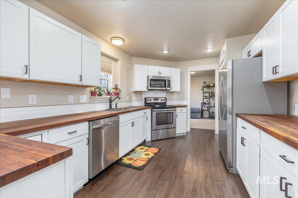 Kitchen with butcher block countertops, white cabinets, appliances with stainless steel finishes, and dark wood-style flooring