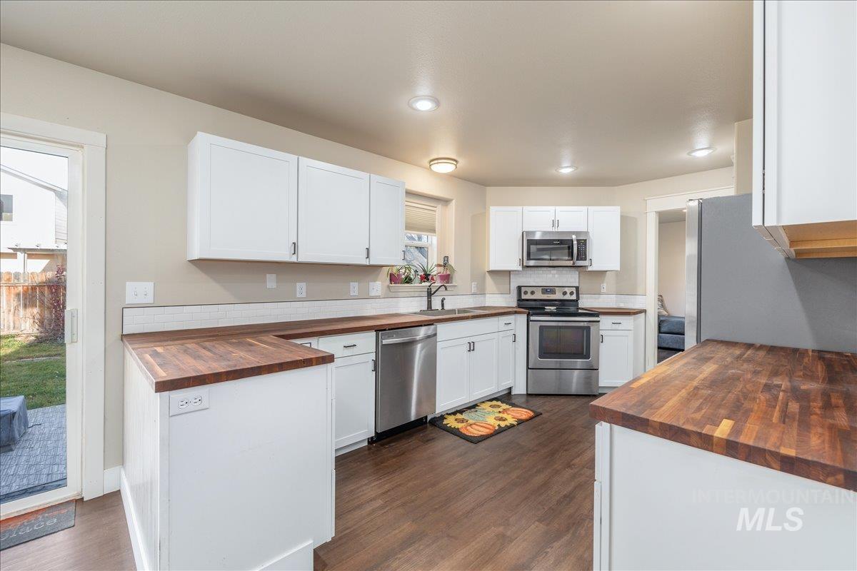 Kitchen featuring butcher block counters, white cabinetry, stainless steel appliances, dark wood-style floors, and recessed lighting