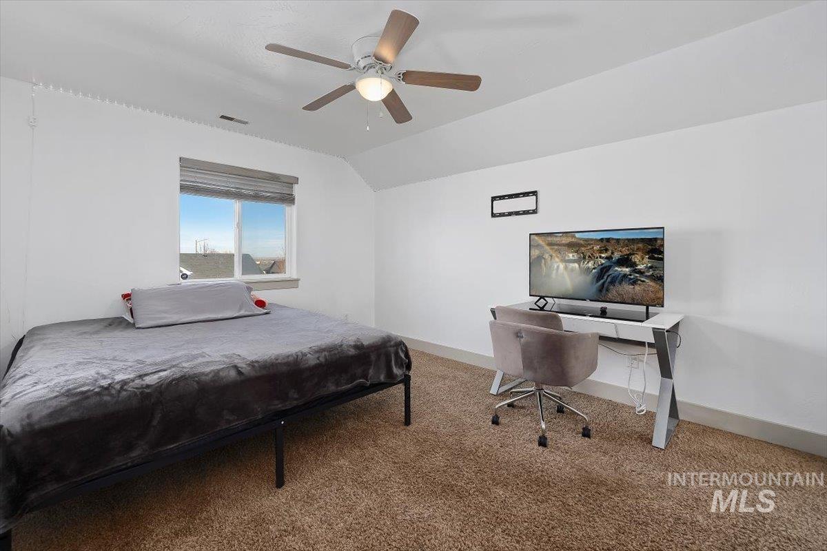 Carpeted bedroom with a ceiling fan, vaulted ceiling, and a desk