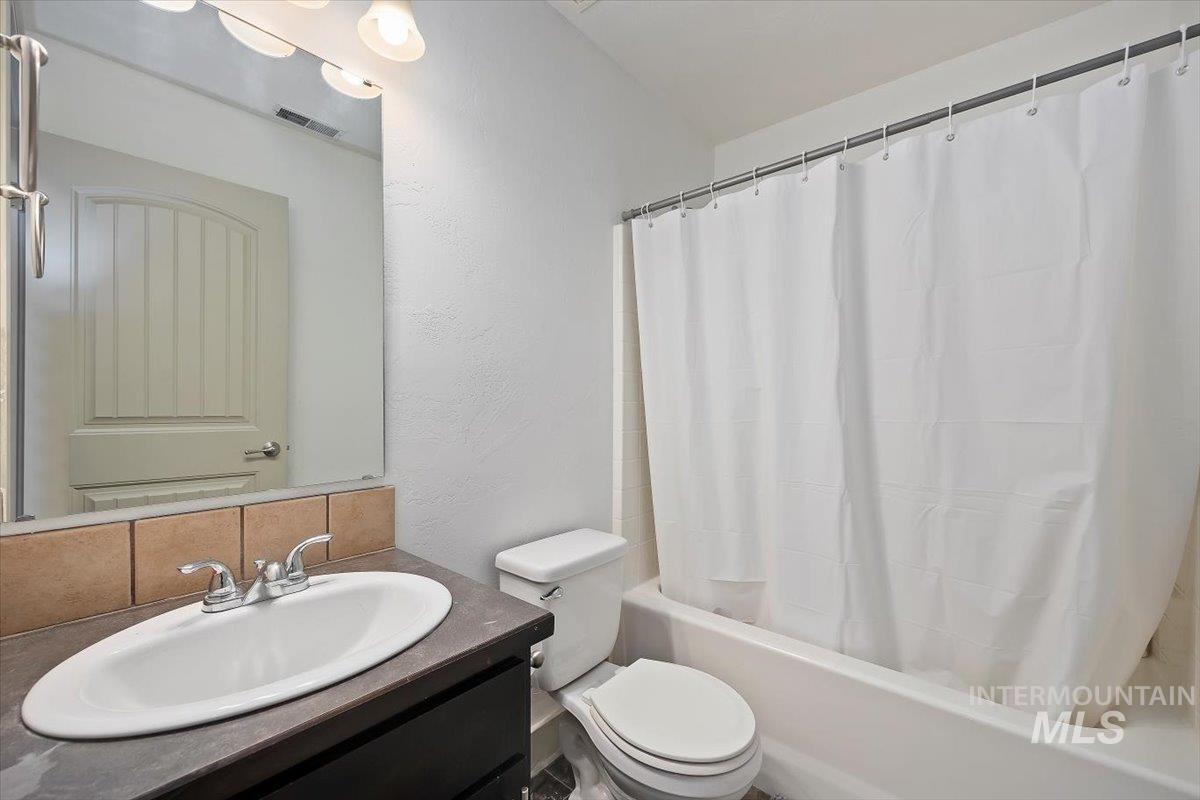 Bathroom featuring vanity, shower / tub combo, backsplash, and a textured wall
