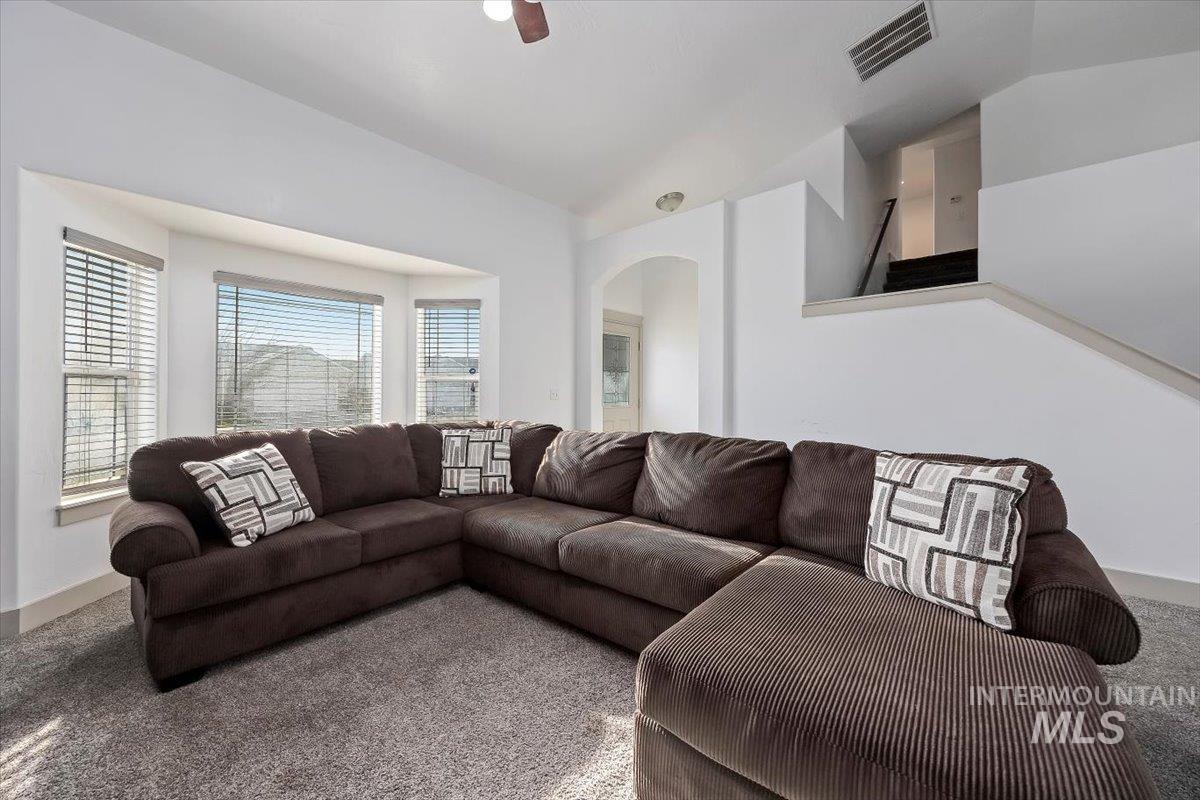 Living area with carpet floors, arched walkways, vaulted ceiling, and a ceiling fan