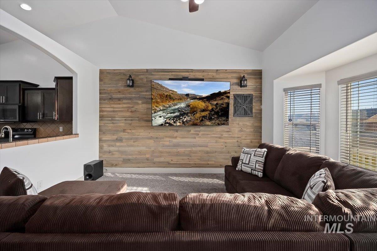 Living area with vaulted ceiling, wood walls, an accent wall, and ceiling fan