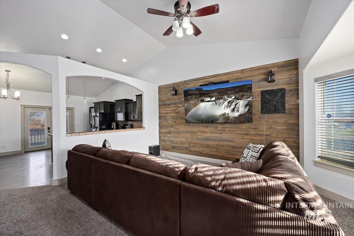 Living area with lofted ceiling, an accent wall, carpet floors, wooden walls, and ceiling fan