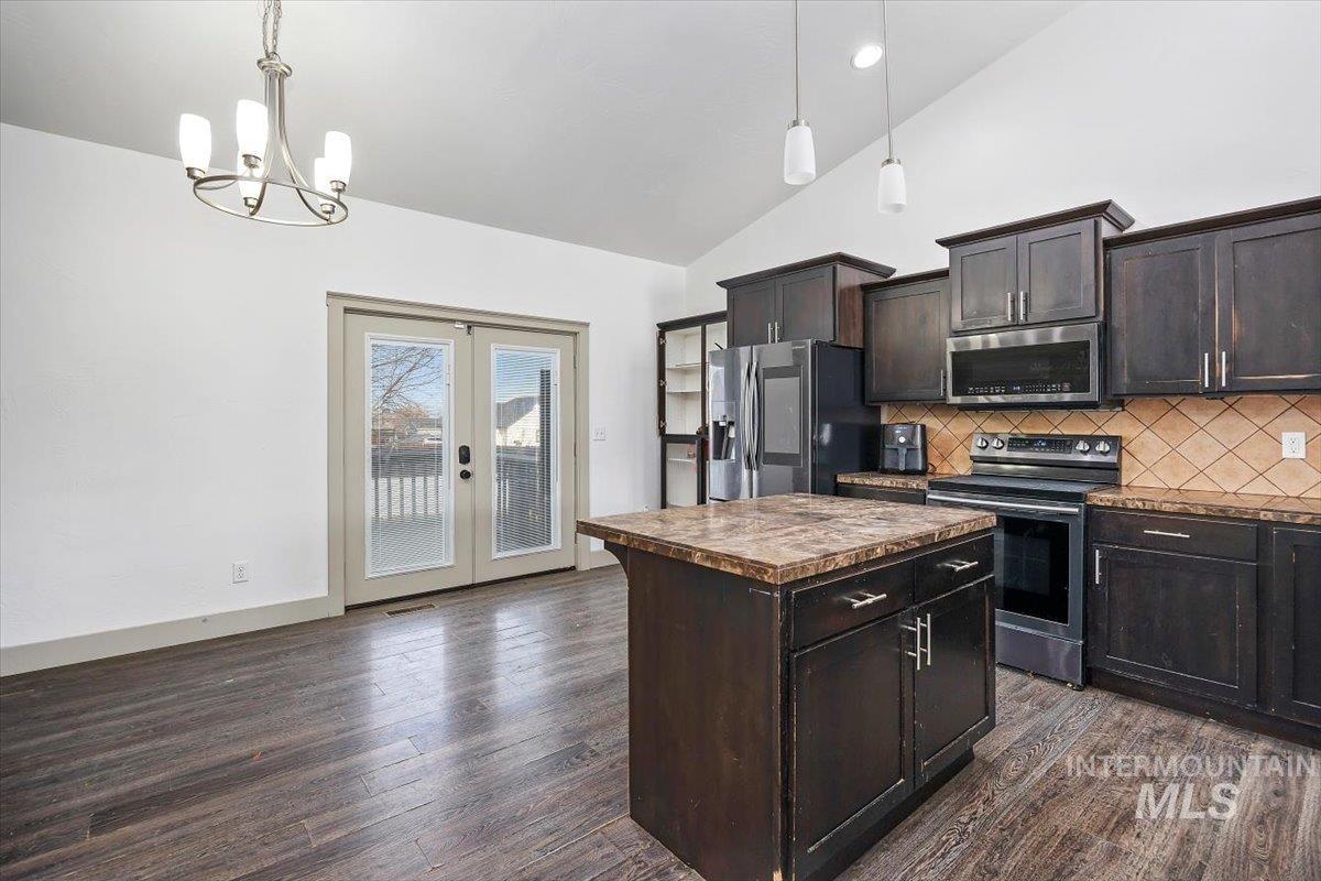 Kitchen featuring appliances with stainless steel finishes, a kitchen island, dark brown cabinets, backsplash, and dark wood finished floors