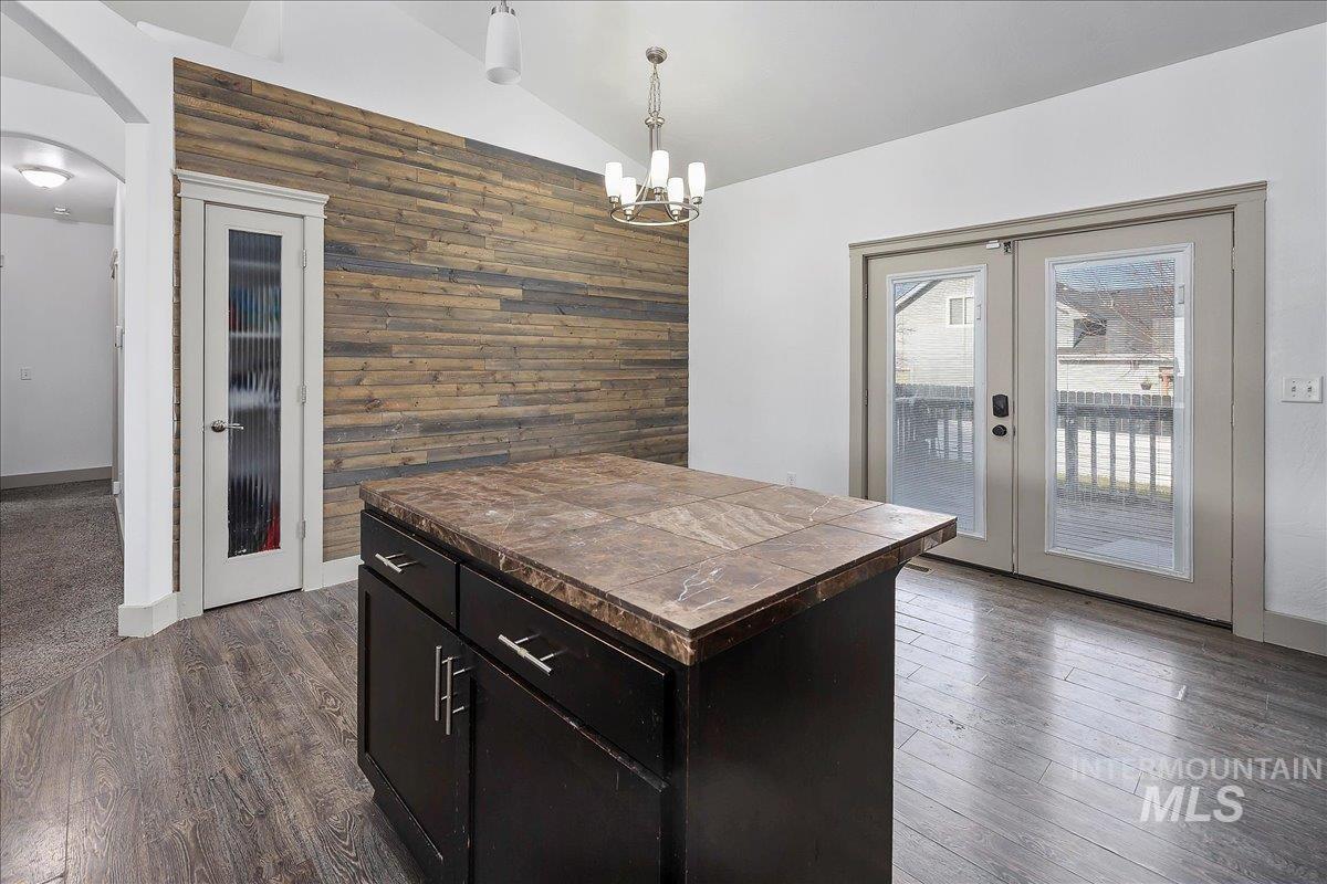 Kitchen with lofted ceiling, french doors, wooden walls, hanging light fixtures, and tile countertops