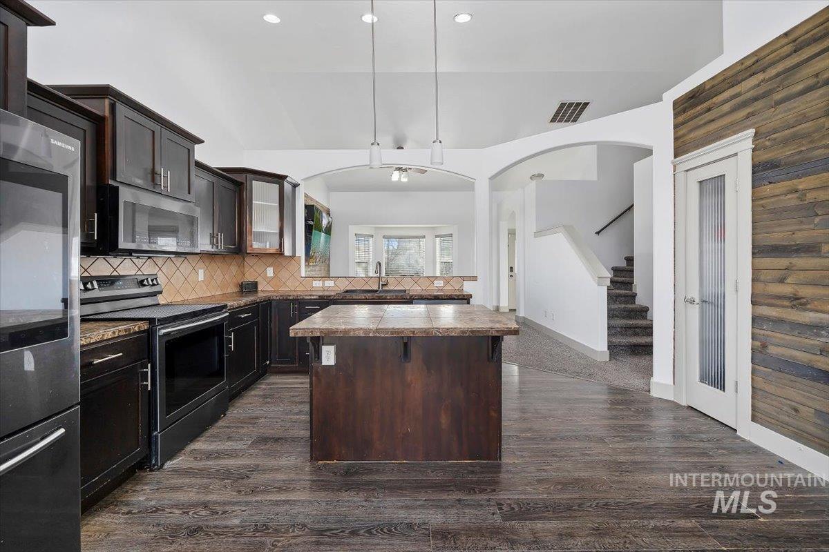 Kitchen with stainless steel appliances, dark brown cabinets, a kitchen island, glass insert cabinets, and dark countertops