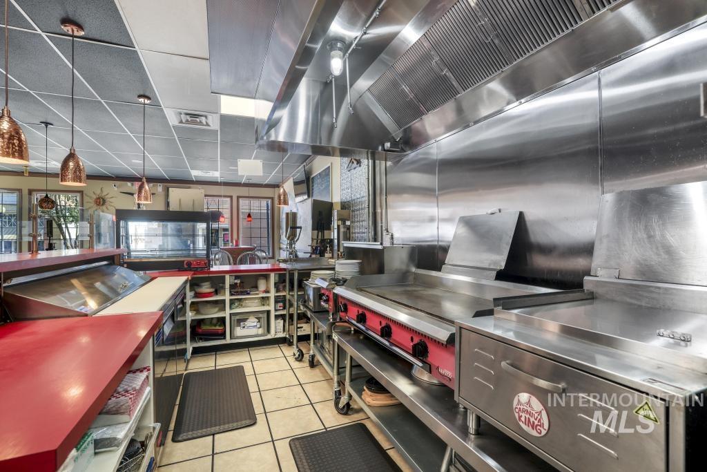 Kitchen featuring stainless steel countertops, wall chimney exhaust hood, light tile patterned flooring, hanging light fixtures, and a paneled ceiling