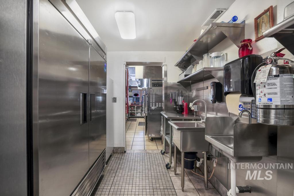 Kitchen featuring stainless steel counters, open shelves, light tile patterned floors, and stainless steel built in fridge