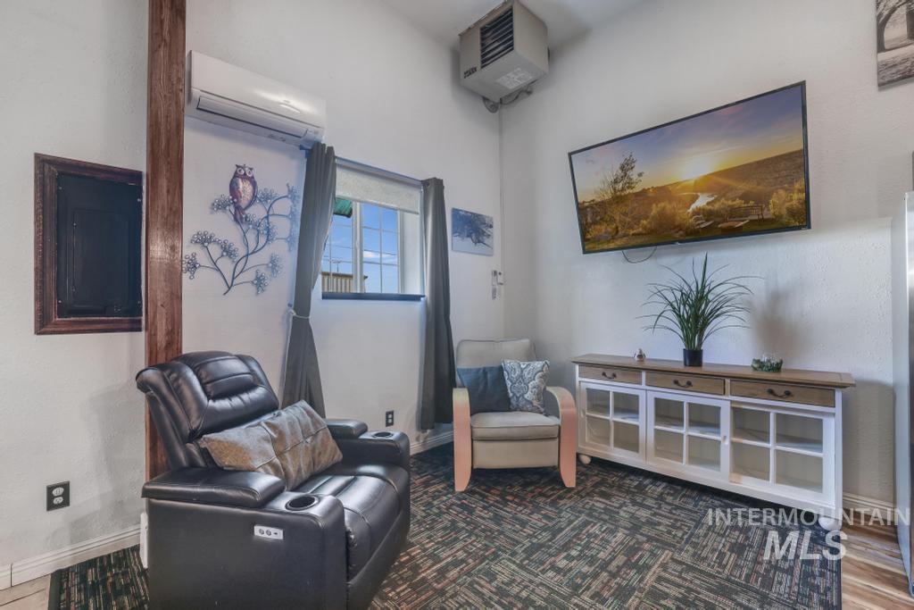 Living area with a heating unit, a wall unit AC, wood finished floors, and electric panel
