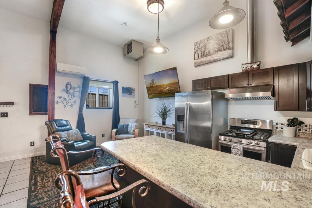 Kitchen with dark brown cabinetry, stainless steel appliances, under cabinet range hood, tile patterned flooring, and pendant lighting