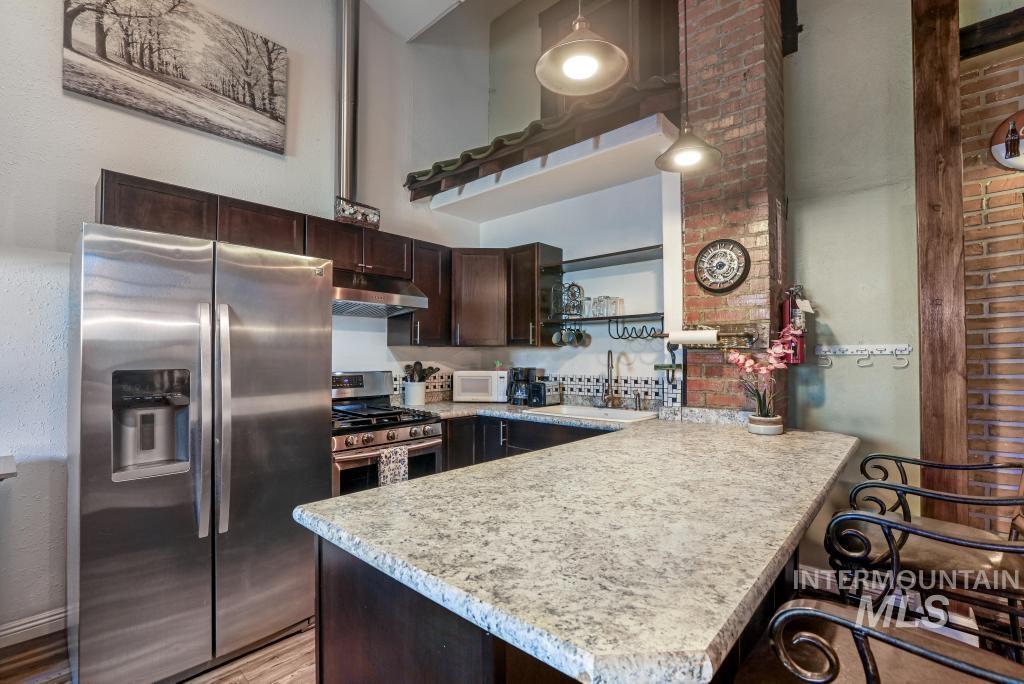 Kitchen featuring dark brown cabinetry, stainless steel appliances, a breakfast bar area, a peninsula, and under cabinet range hood