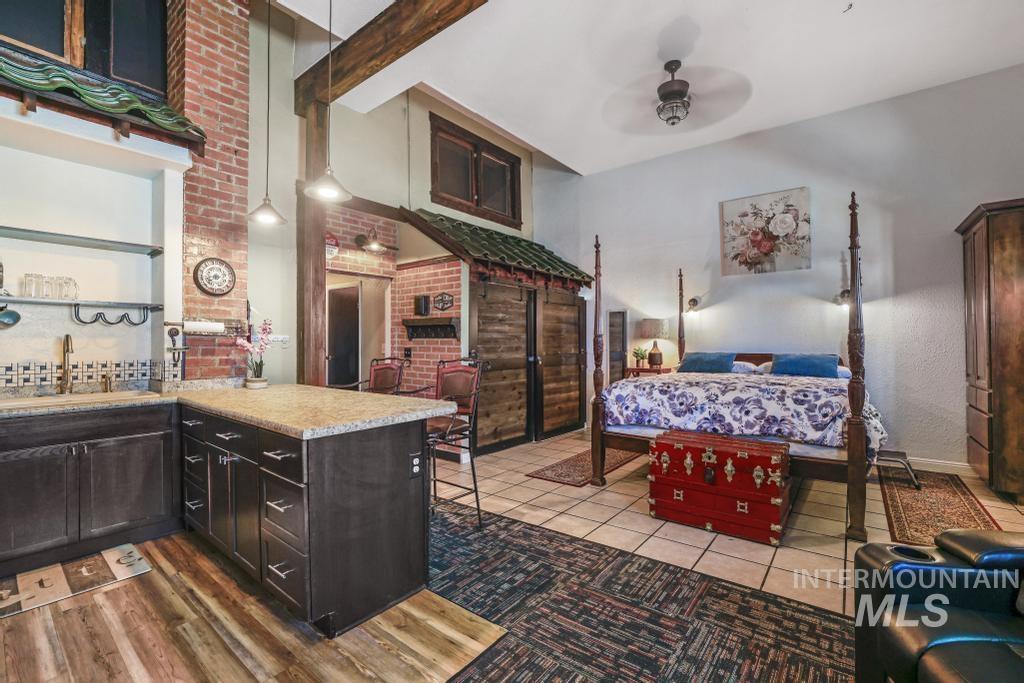 Bedroom with beam ceiling, brick wall, light tile patterned floors, and ceiling fan