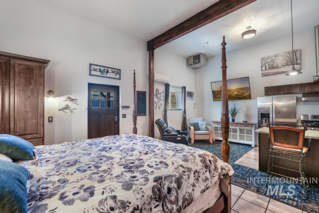 Bedroom featuring dark tile patterned flooring, beamed ceiling, and stainless steel fridge with ice dispenser