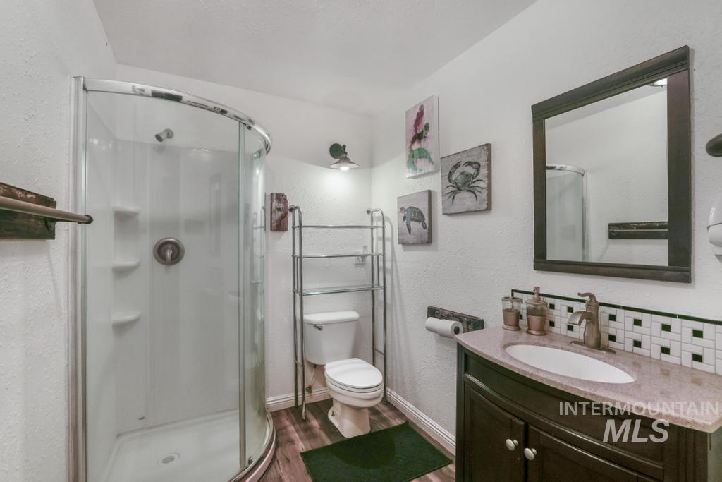 Bathroom with a textured wall, vanity, a shower stall, and dark wood-style floors