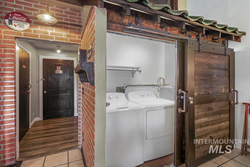 Washroom featuring light tile patterned flooring, brick wall, and washing machine and dryer