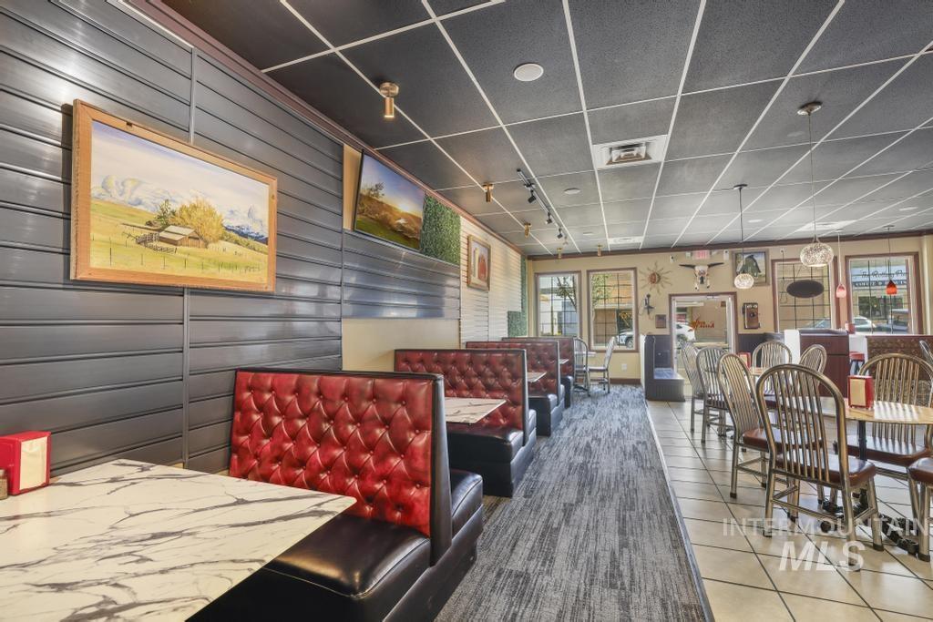 Dining space featuring light tile patterned flooring, a drop ceiling, and wood walls