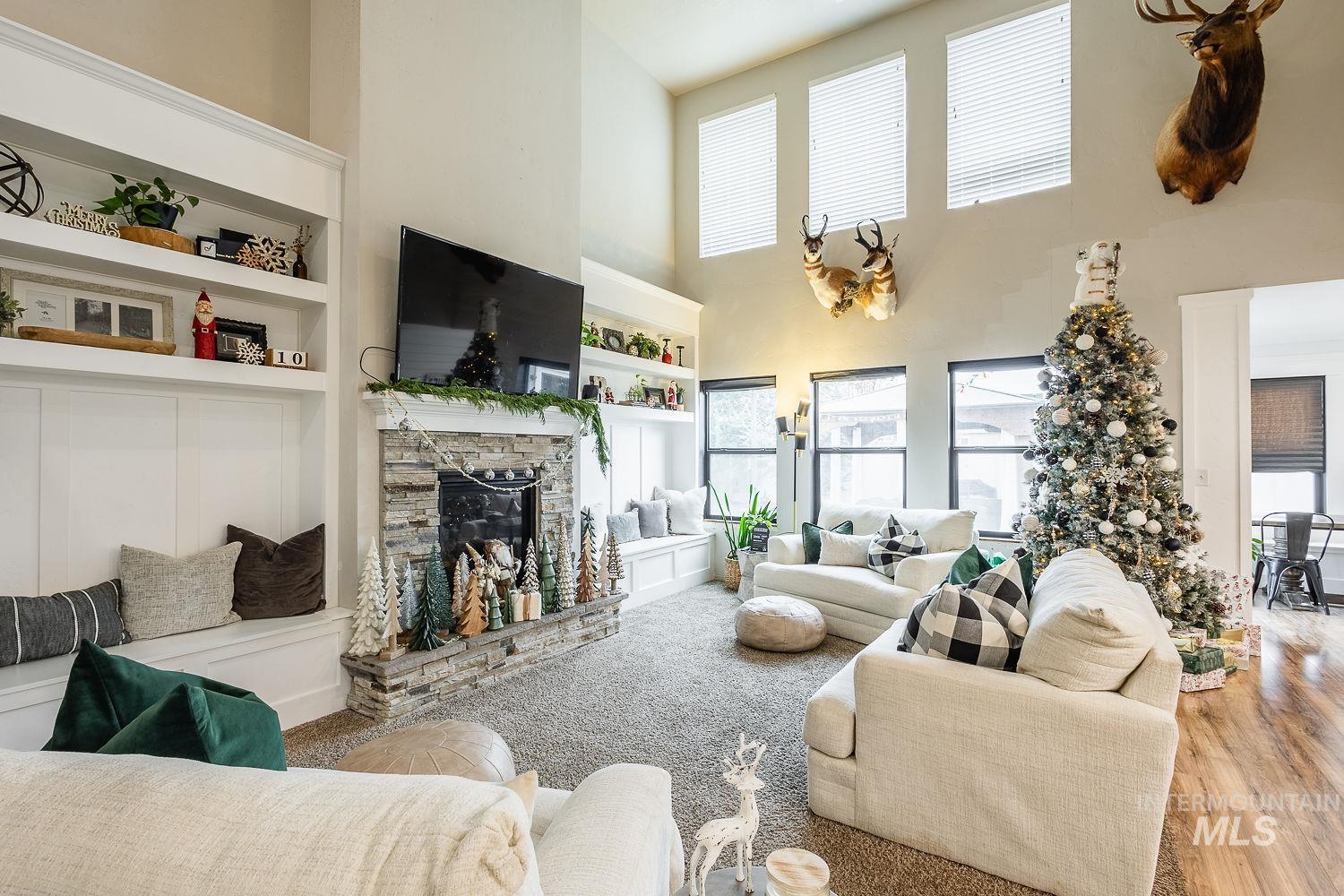 Living area featuring built in features, a stone fireplace, wood finished floors, and a high ceiling
