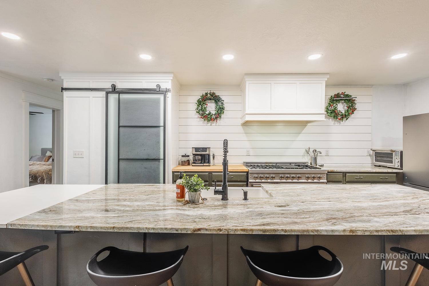 Kitchen with a kitchen bar, light stone counters, white cabinetry, recessed lighting, and custom range hood