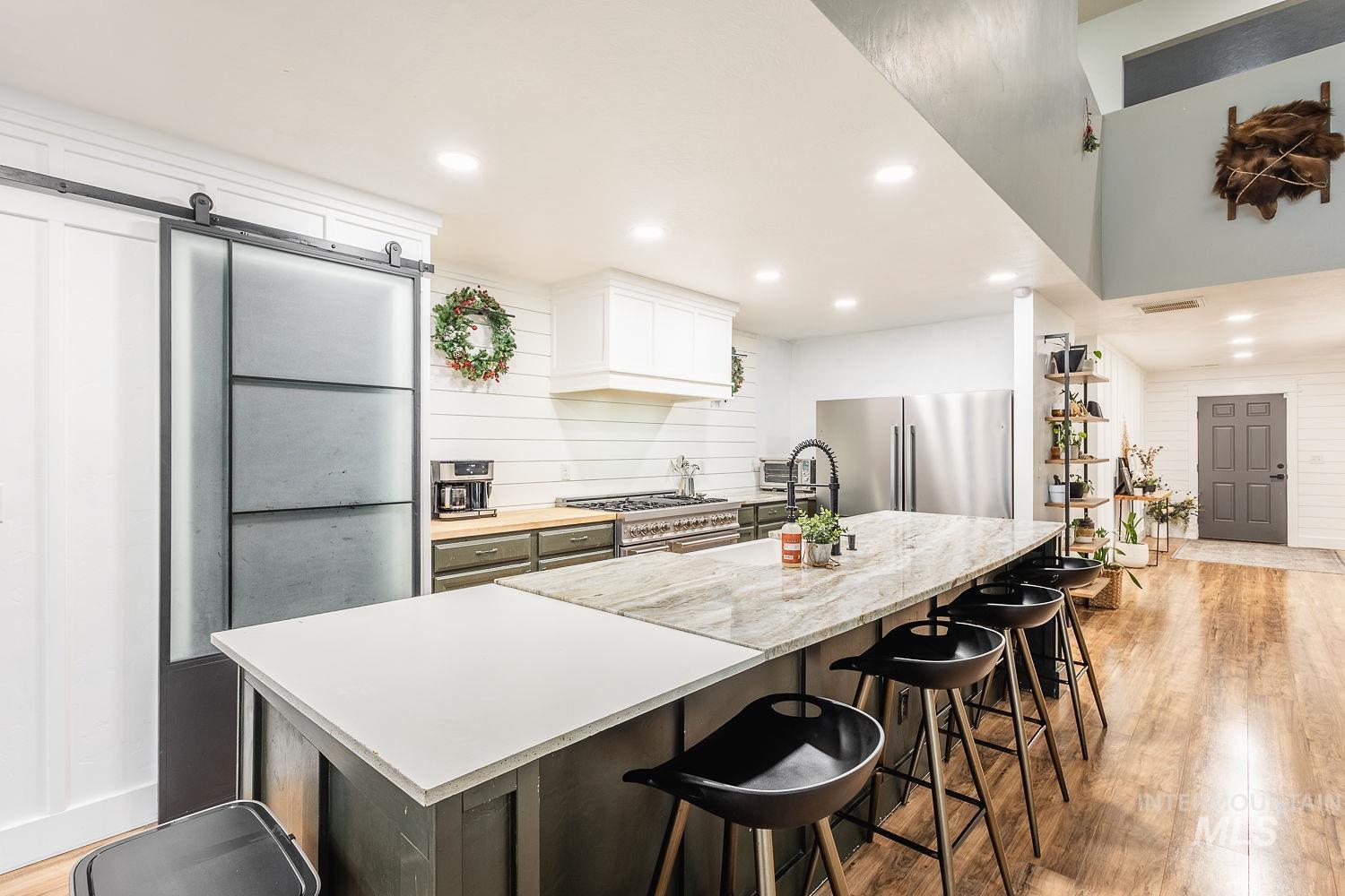 Kitchen with a barn door, light wood-style floors, freestanding refrigerator, an island with sink, and a kitchen bar