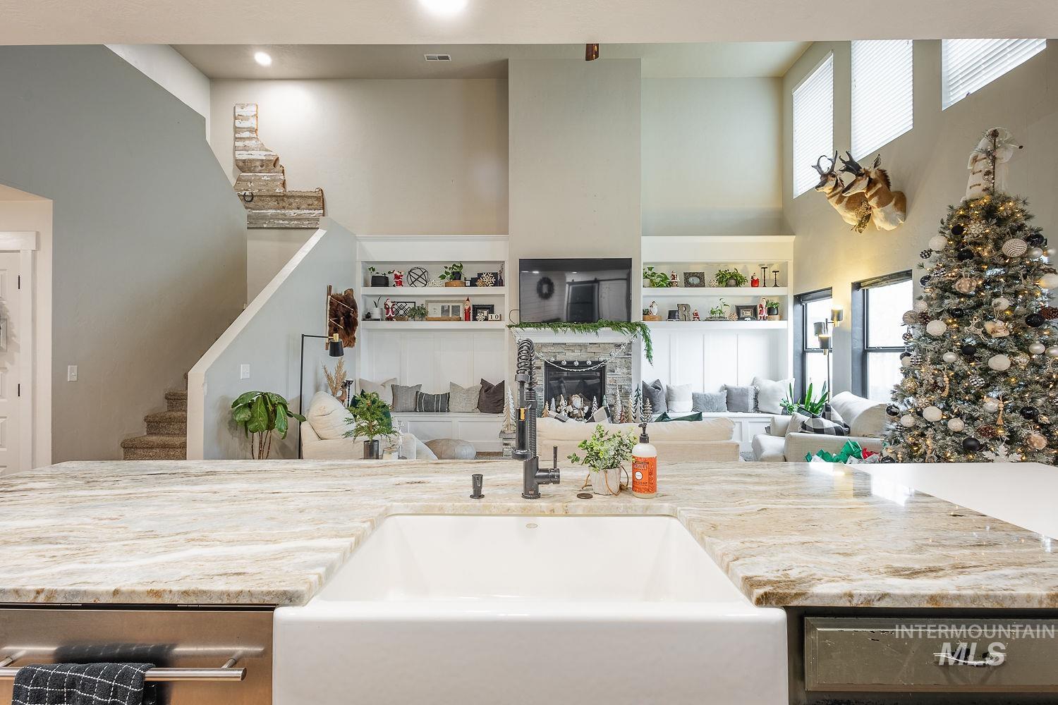 Kitchen with light stone countertops, a stone fireplace, a towering ceiling, and built in shelves