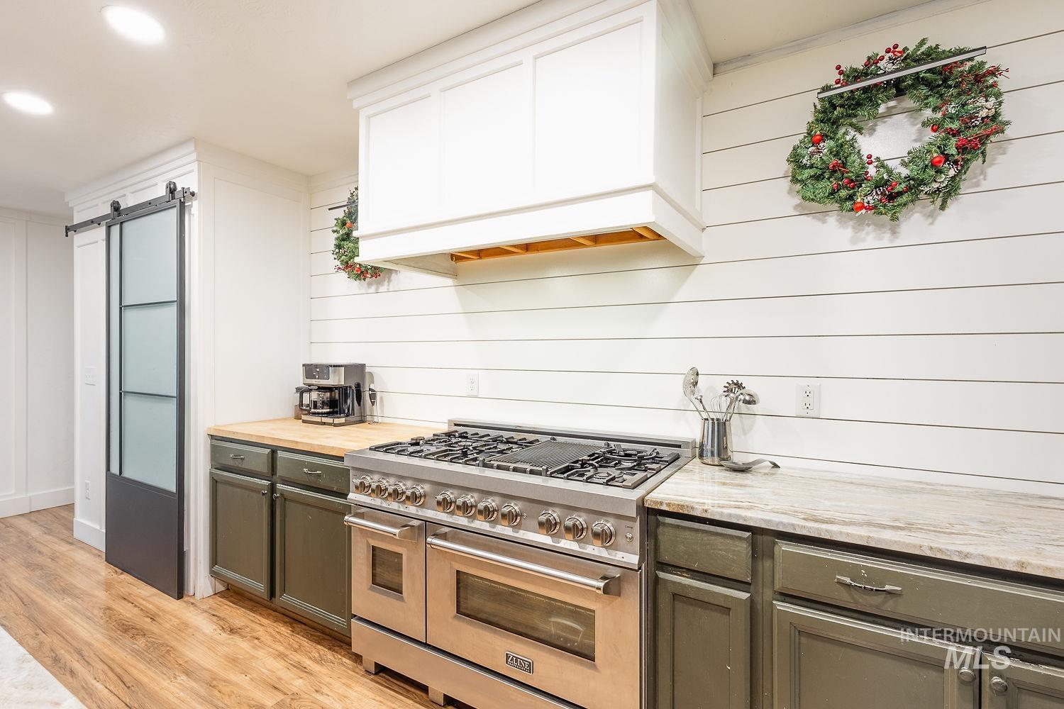 Kitchen featuring double oven range, a barn door, light wood-style floors, custom range hood, and butcher block counters