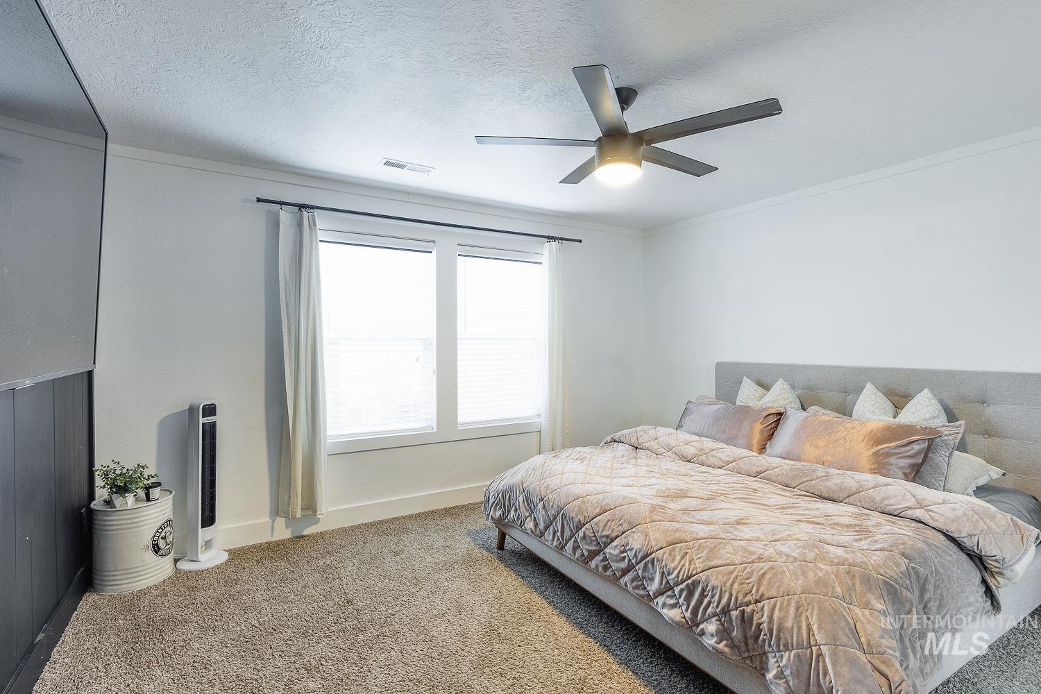 Carpeted bedroom with ornamental molding, a textured ceiling, and ceiling fan