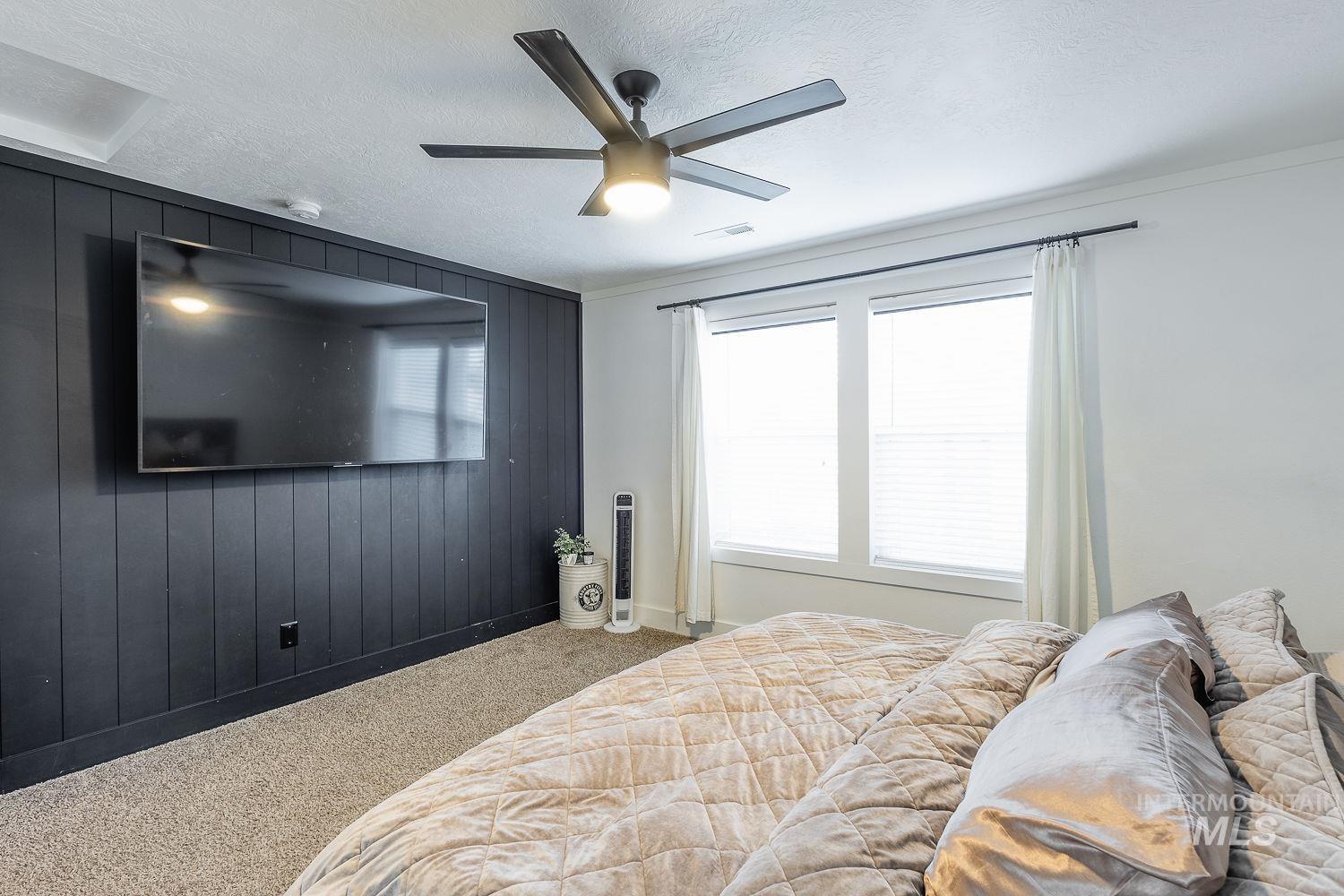 Bedroom with wood walls, carpet, ceiling fan, a textured ceiling, and an accent wall
