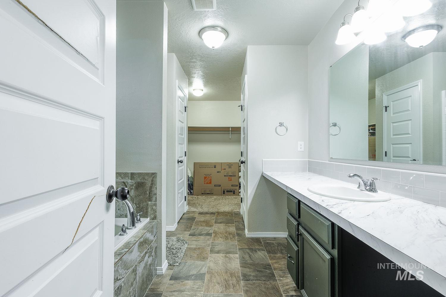 Bathroom with vanity, a walk in closet, a textured ceiling, tiled bath, and stone finish flooring