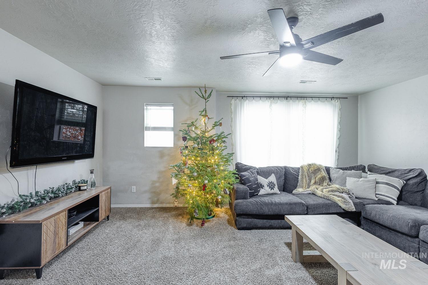 Living room with a textured ceiling, carpet flooring, and ceiling fan