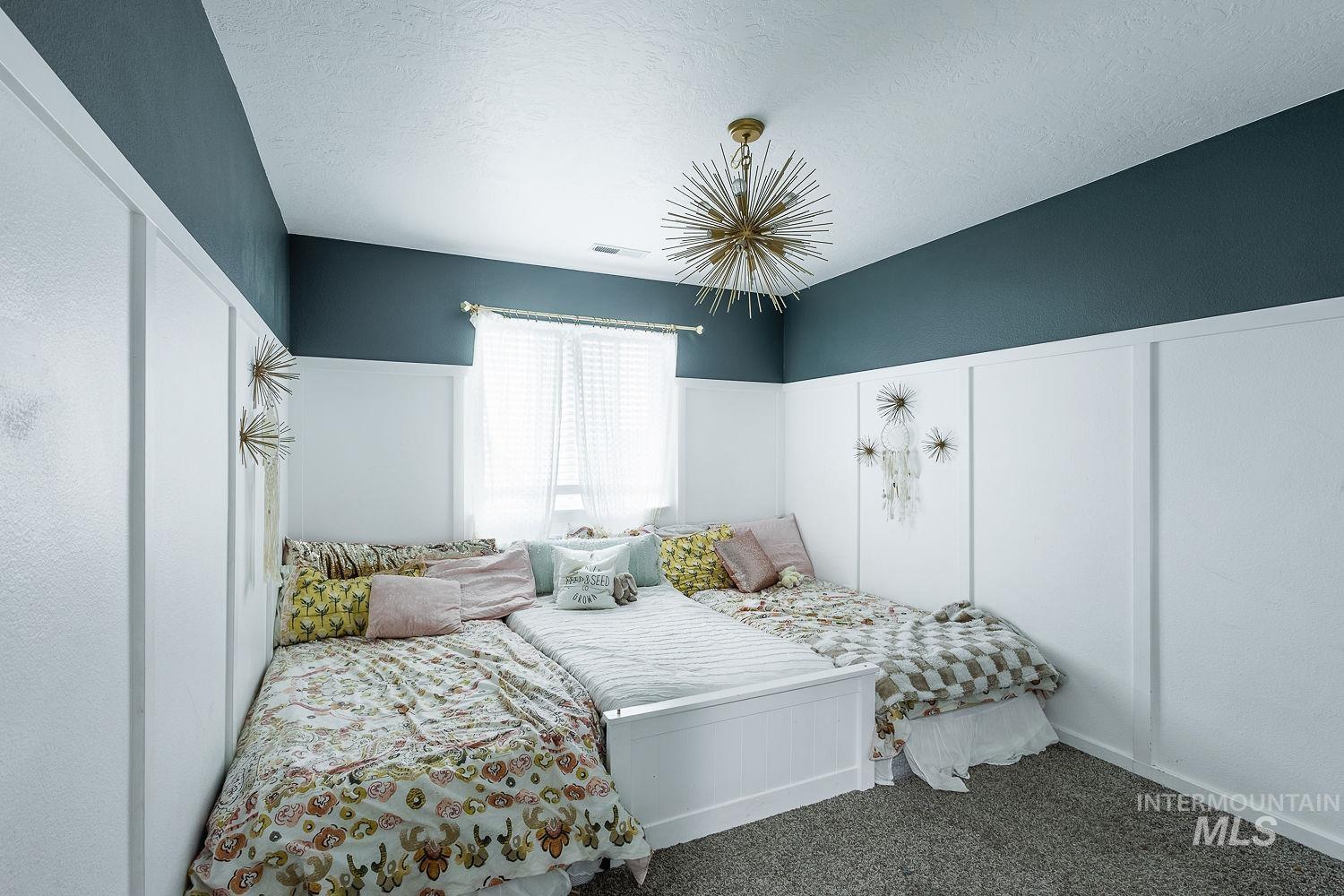 Carpeted bedroom featuring a textured ceiling, a decorative wall, a wainscoted wall, and a chandelier
