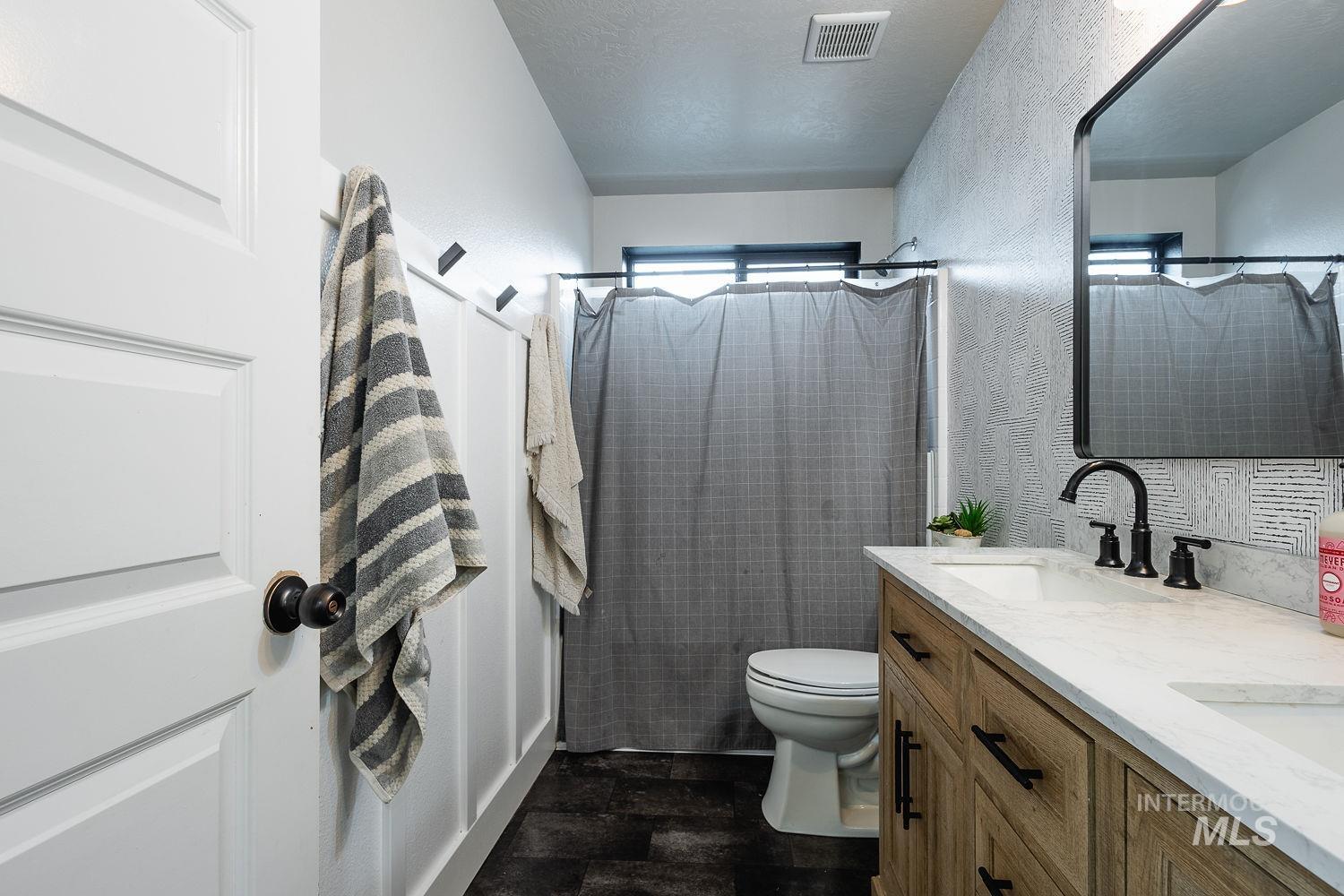 Bathroom with a shower stall, double vanity, a textured ceiling, and a textured wall