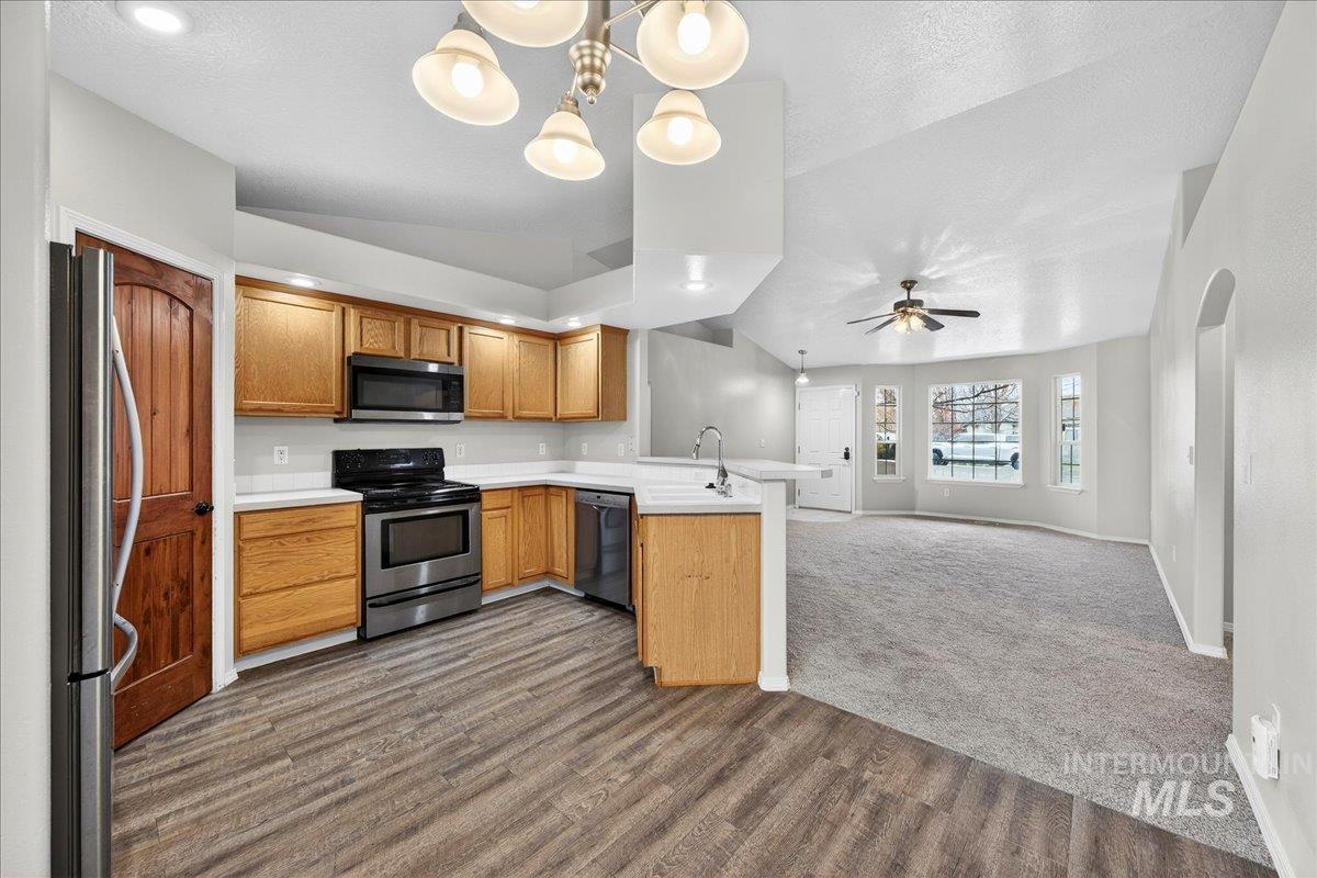 Kitchen with vaulted ceiling, light countertops, stainless steel appliances, hanging light fixtures, and a peninsula