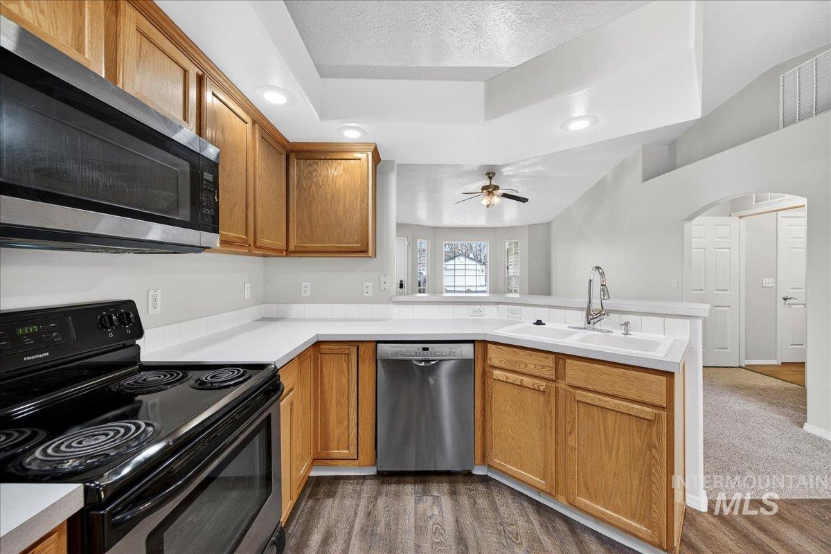 Kitchen with appliances with stainless steel finishes, a peninsula, a textured ceiling, brown cabinets, and recessed lighting