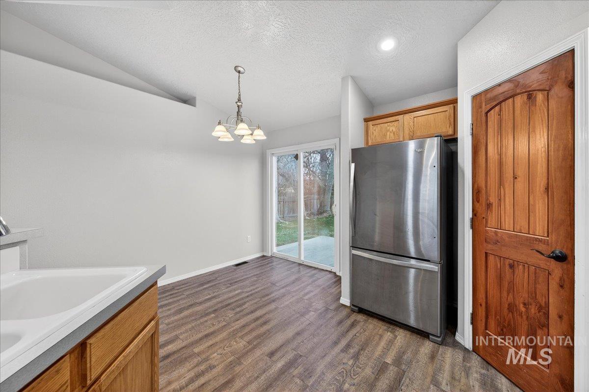 Kitchen with freestanding refrigerator, a textured ceiling, brown cabinetry, pendant lighting, and vaulted ceiling