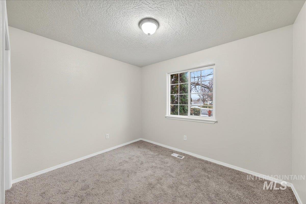 Carpeted empty room with a textured ceiling and baseboards