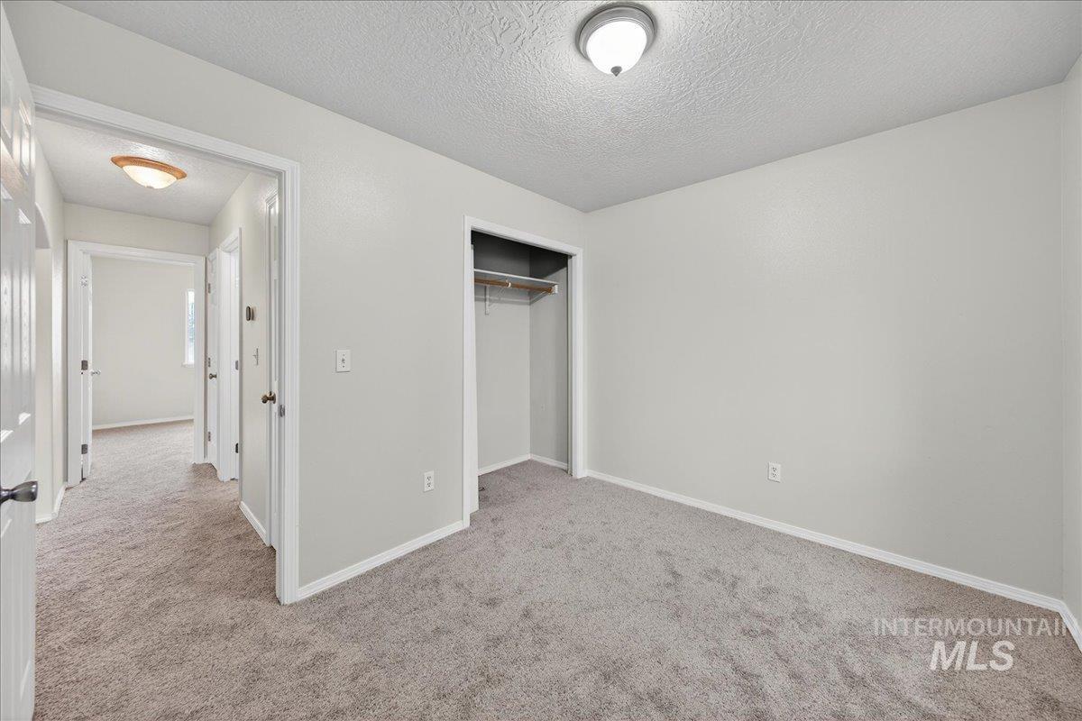 Unfurnished bedroom featuring light colored carpet, a textured ceiling, and a closet