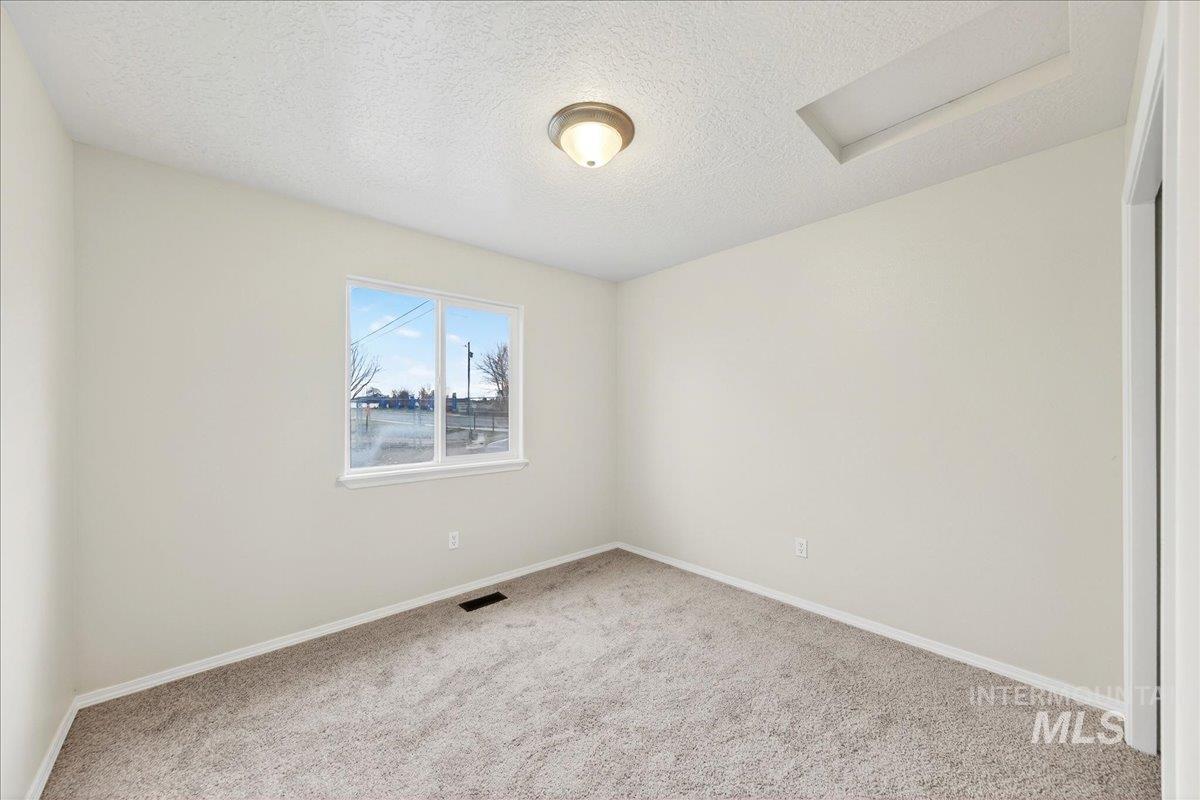 Carpeted empty room featuring attic access and a textured ceiling