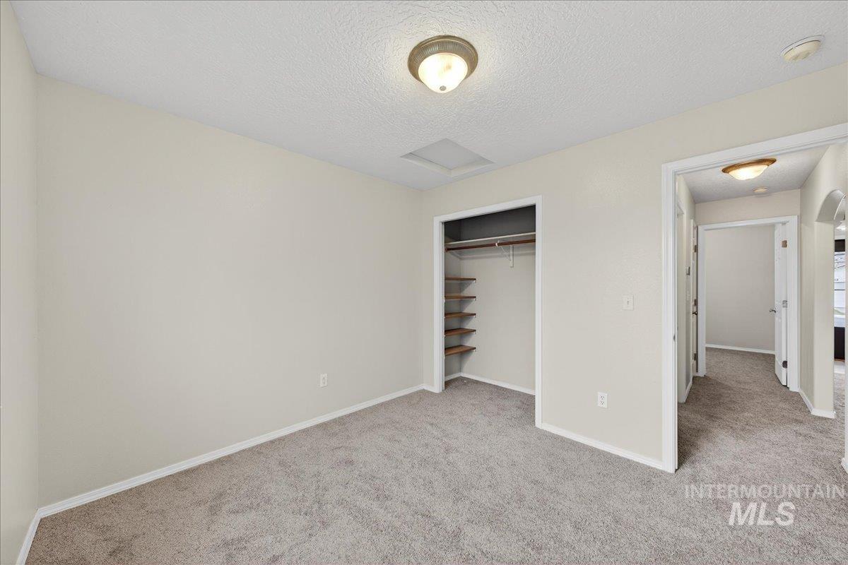 Unfurnished bedroom with a textured ceiling, light carpet, and a closet