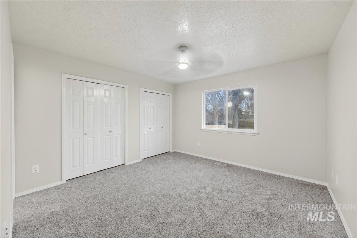 Unfurnished bedroom with a textured ceiling, two closets, carpet floors, and a ceiling fan