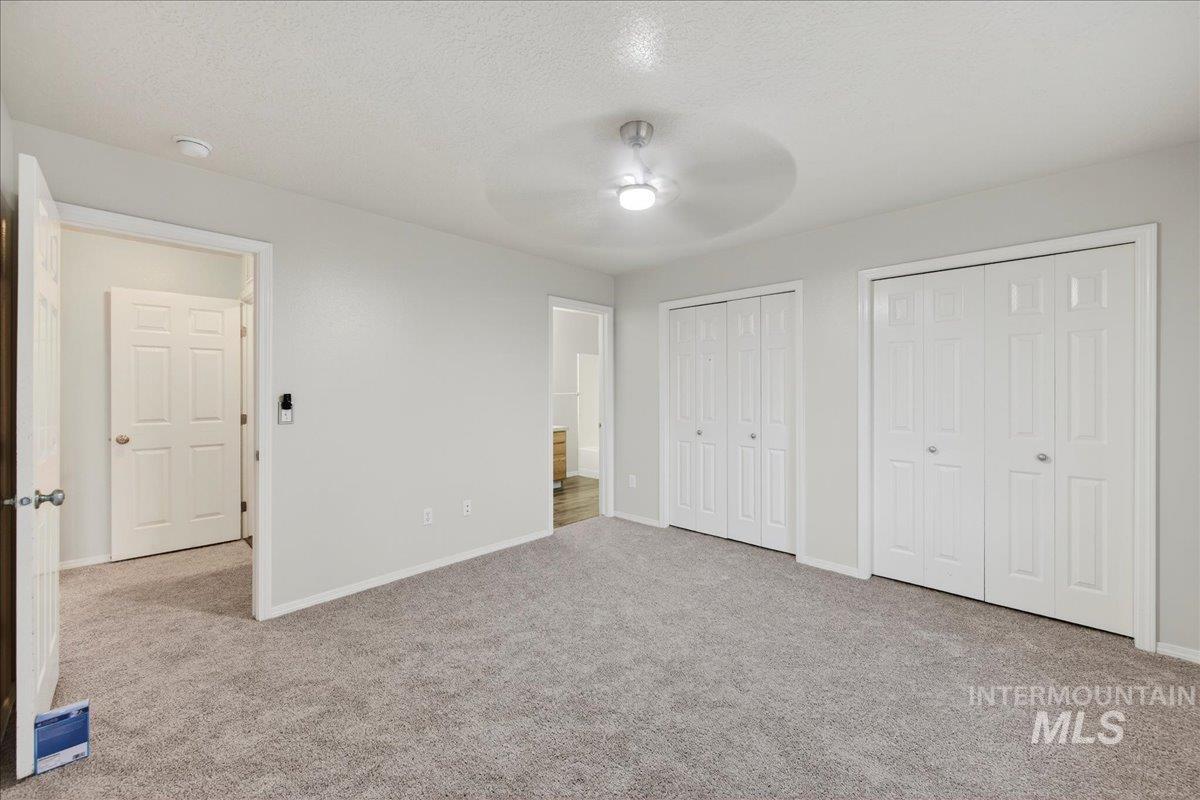 Unfurnished bedroom featuring multiple closets, a textured ceiling, light carpet, and a ceiling fan