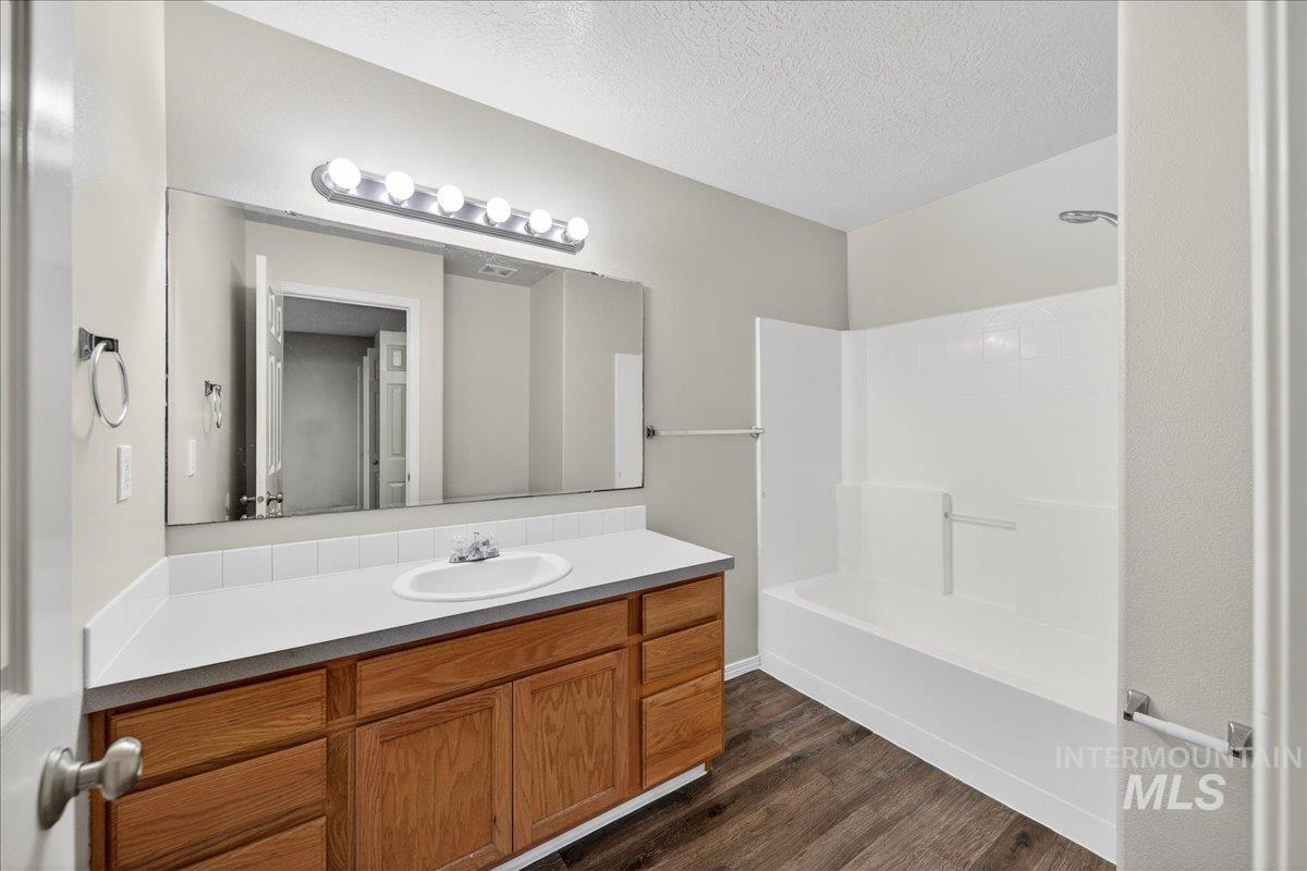 Bathroom with vanity, shower / tub combination, a textured ceiling, and dark wood-style flooring